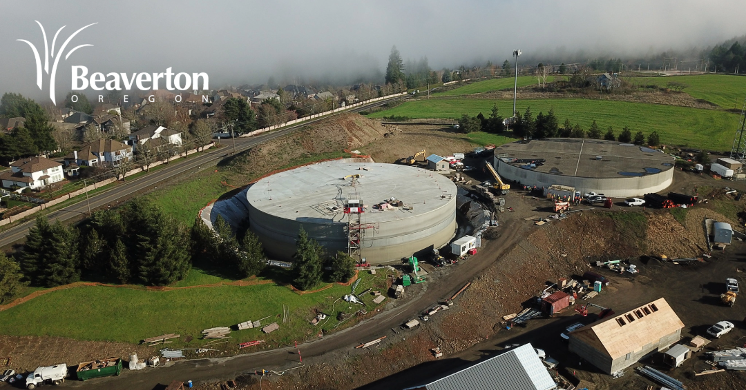Photograph of a large concrete water reservoir with an access road in the foreground. Beaverton, Oregon logo