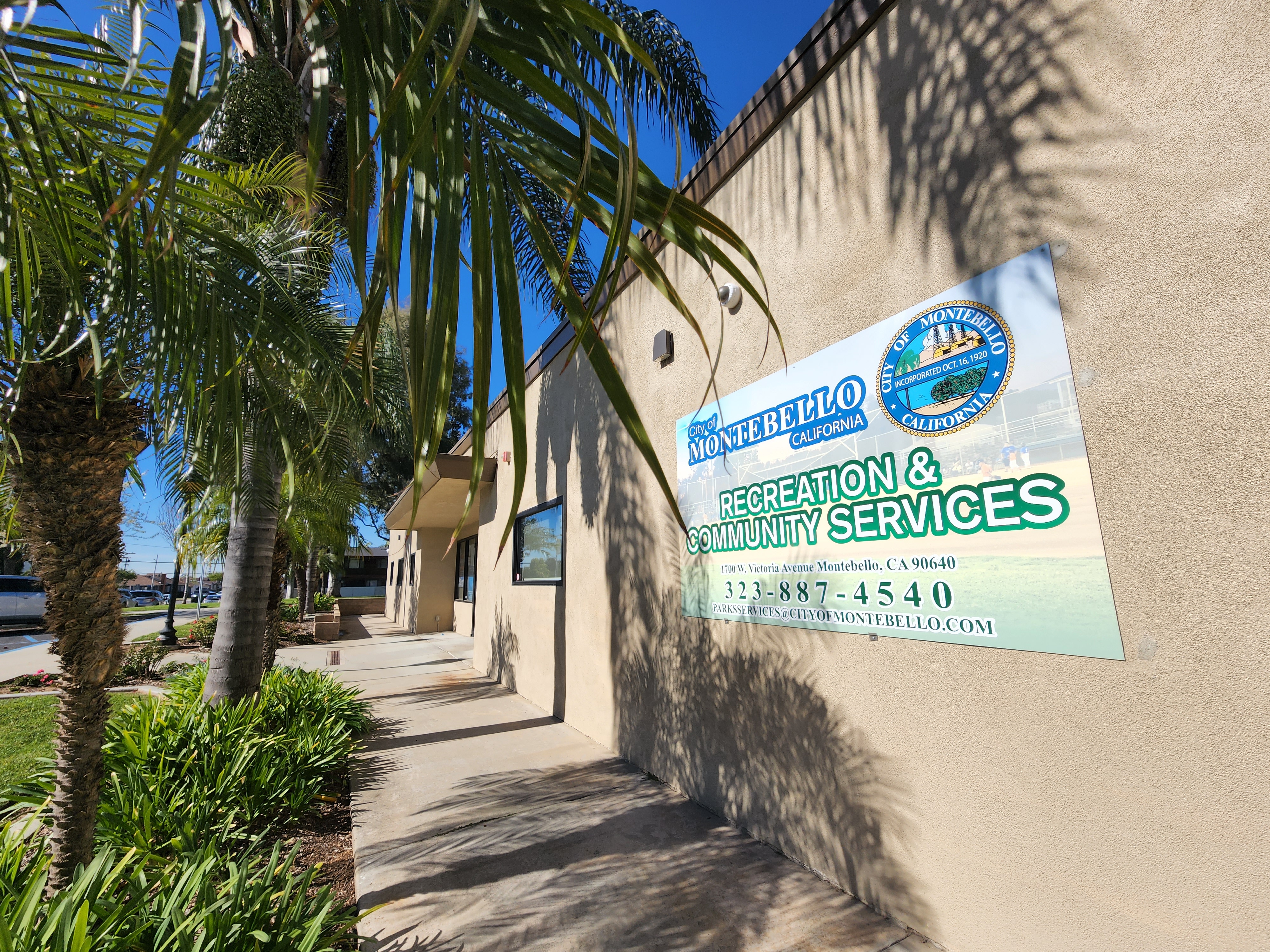 A building exterior with palm trees and a sign for Montebello's Recreation & Community Services. Clear blue sky in the background.