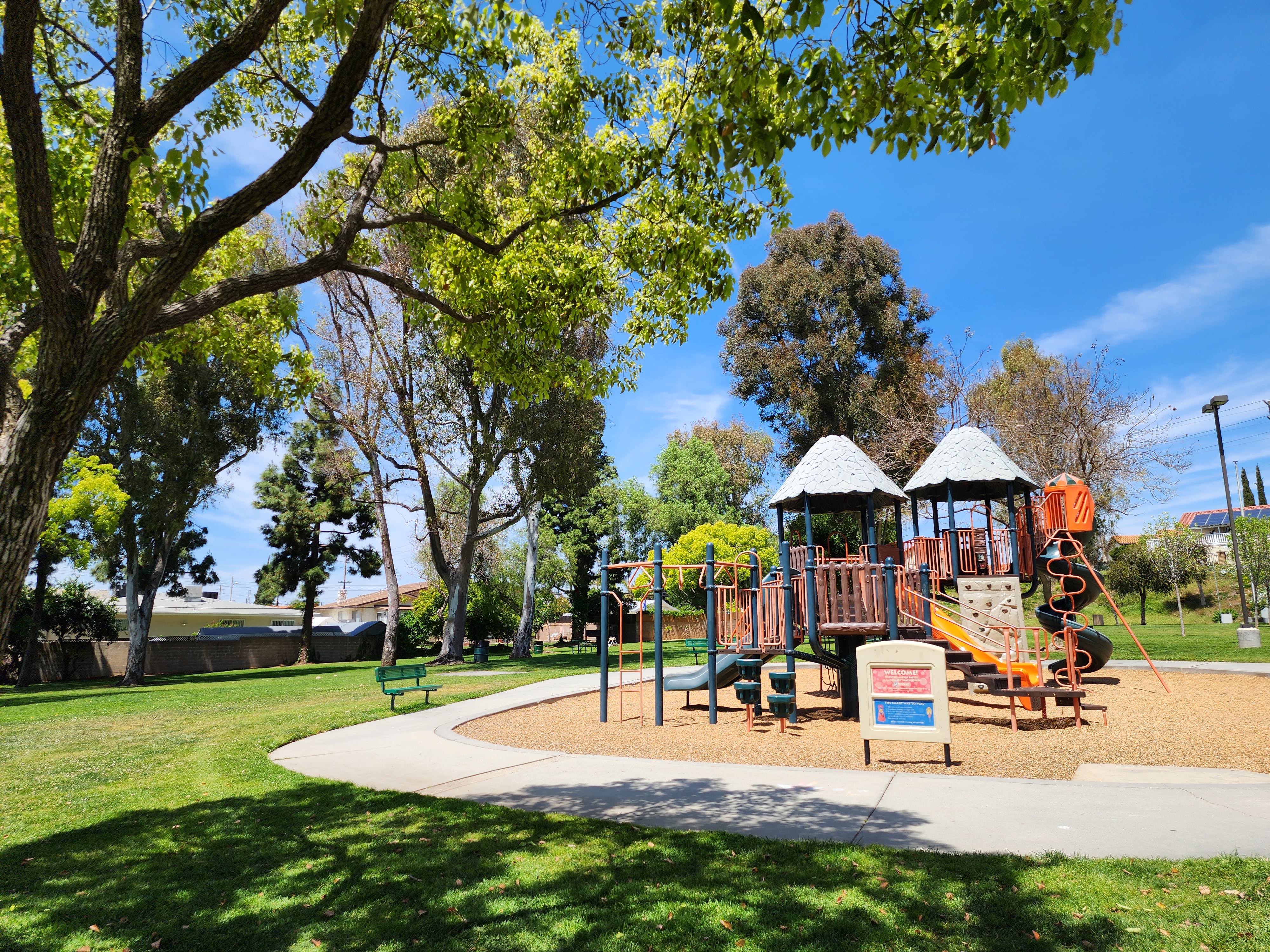 A playground with slides and climbing structures surrounded by trees and green grass under a clear blue sky.